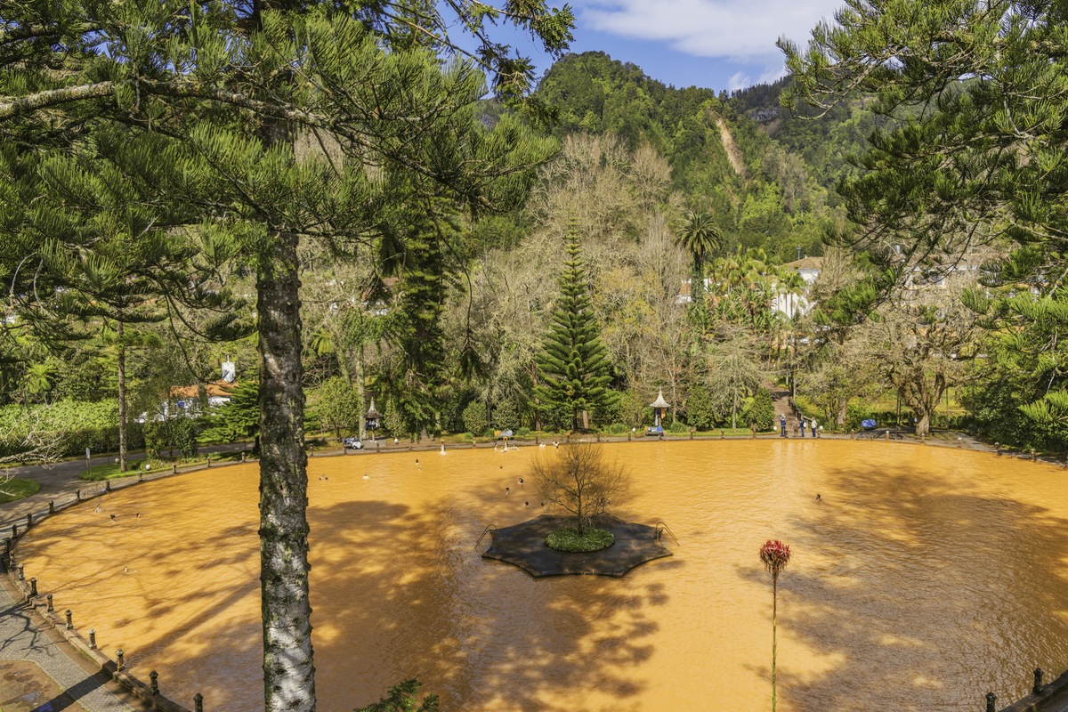 The rust-colored thermal pool surrounded by trees at Parque Terra Nostra in Furnas