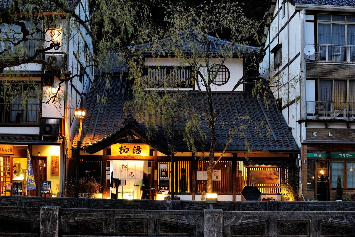 An illuminated bathhouse and riverside street in Kinosaki Onsen, Japan