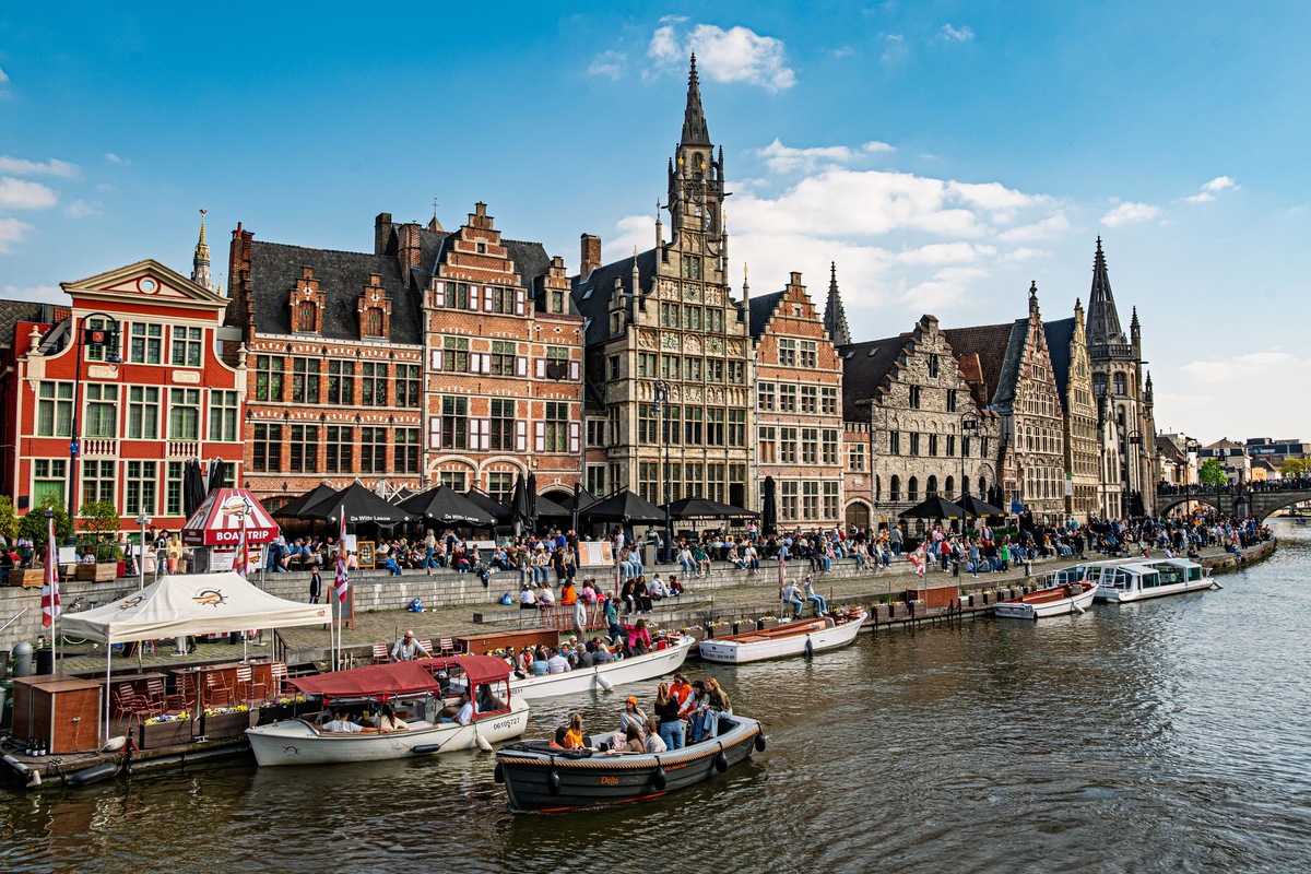 Historic gabled buildings, visitors and boats along the Graslei waterfront in Ghent